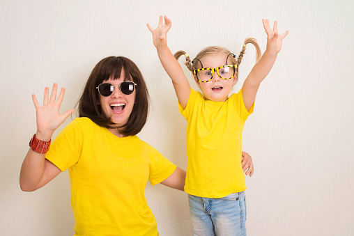 Portrait funky crazy hipsters girls in funny eyeglasses and yellow t-shirts laugh open mouth having fun together.