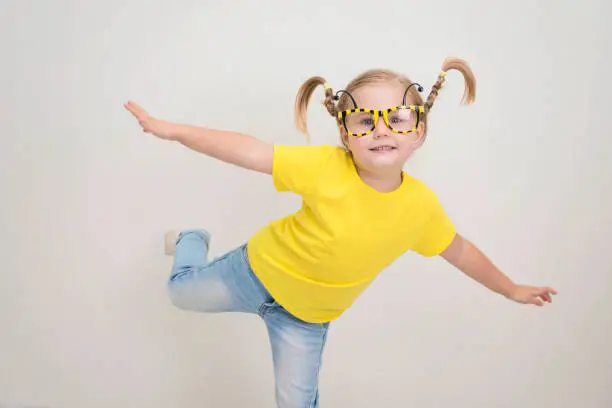 Photo of Happy funny little girl in party bee eyeglasses with funny pigtails braids in yellow t-shirt and jeans.