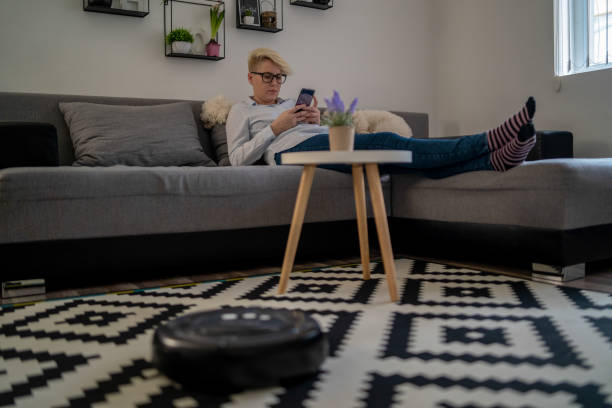 istock Robotic vacuum cleaner cleaning the room while woman resting on sofa, closeup 1214555332