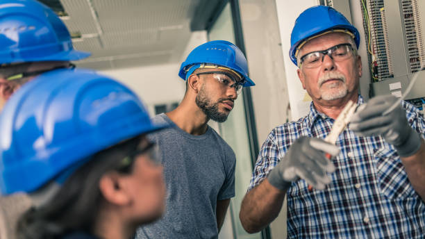 istock Senior electrician cutting a wire in front of his students 1214561869