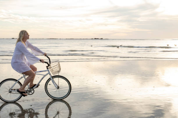 istock Woman rides bicycle down beach at sunrise 1214564992