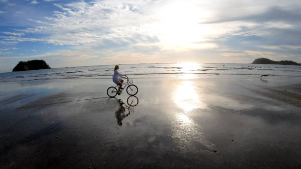 istock Woman rides bicycle down beach at sunrise 1214565177