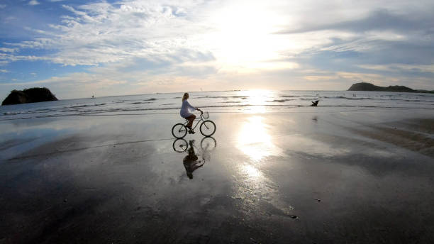 istock Woman rides bicycle down beach at sunrise 1214565218