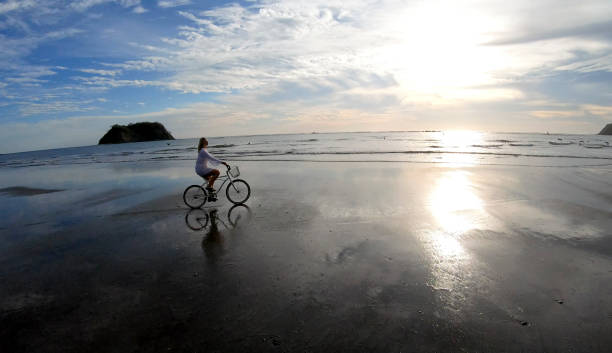 istock Woman rides bicycle down beach at sunrise 1214565234