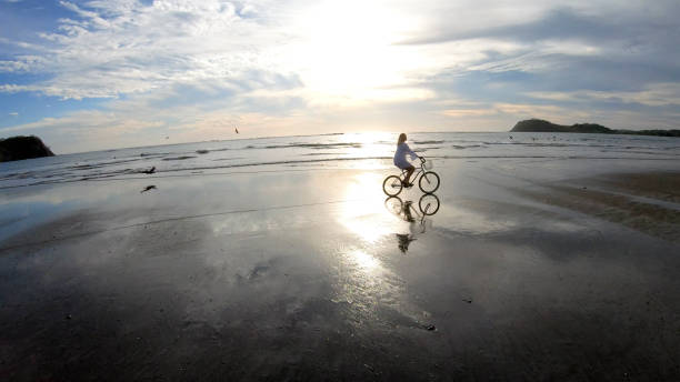 istock Woman rides bicycle down beach at sunrise 1214565251