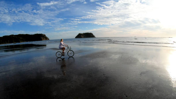 istock Woman rides bicycle down beach at sunrise 1214565263