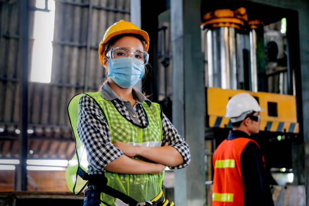 fabrikfrau arbeiterin oder technikerin mit hygienischer maske steht mit selbstbewusstem handeln mit ihrem mitarbeiter als hintergrund - fabrik fotos stock-fotos und bilder