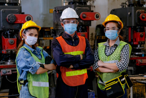 gruppe von arbeitern und arbeitern mit maskenständer mit selbstbewusstem handeln am fabrikarbeitsplatz und verschiedenen maschinen als hintergrund - preventative maintenance stock-fotos und bilder