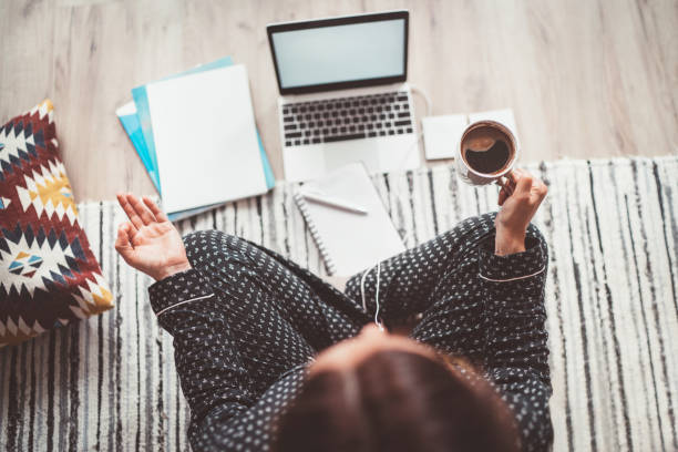 Businesswoman dressed in pajamas meditating with morning coffee with Gyan Mudra palms.On the floor office with laptop, papers top view shot. Distance work in worldwide quarantine time concept. una mujer de negocios vestida con pijamameditando con café de la mañana con palmas de gyan mudra. en la oficina del piso con computadora portátil, papeles de primera vista. trabajo a distancia en el concepto mundial de tiempo de cuarentena.