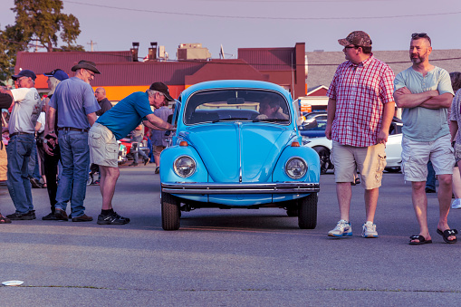 Dartmouth, Nova Scotia, Canada - July 4, 2019 : Classic Volkswagen Beetle at weekly summer A&W Cruise-In at Woodside ferry terminal parking lot, Dartmouth, Nova Scotia, Canada. Driver stops to speak with a man while people walk among the classic cars and socialize on a beautiful summer evening.