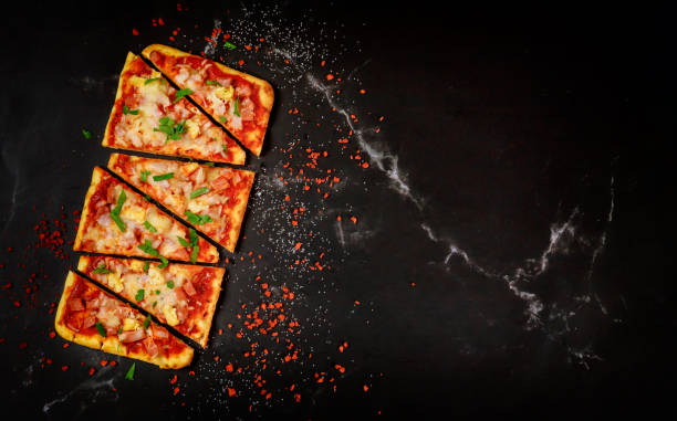 Sliced Hawaiian pizza on black stone background, top view. Sliced Hawaiian pizza with ham and pineapple on black stone background, top view. flatbread stock pictures, royalty-free photos & images