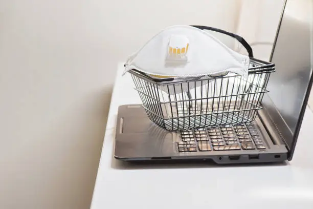 Conceptual photo with miniature shopping-basket and protecting mask and glasses. Safety internet shopping.