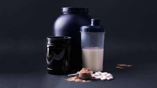 Sports nutrition supplements on a black background. Fitness, bodybuilding, healthy lifestyle concept. Whey protein powder in measuring scoop. Copy space Sports nutrition supplements on a black background. Fitness, bodybuilding, healthy lifestyle concept. Whey protein powder in measuring scoop. Copy space bodybuilding supplement stock pictures, royalty-free photos & images