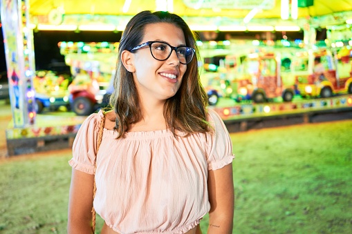 Young beautiful woman wearing glasses smiling happy and excited at funfair around lights at night
