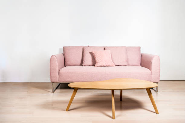 A pink sofa with metal frame and an oak coffee table in front of a white wall, over light hard wood floors. Copy space on the wall.