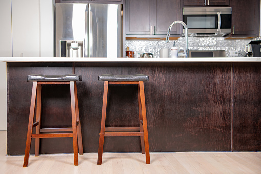 Close up of two bar stools at a kitchen bar, with a white quartz countertop. Stainless steel appliances behind.