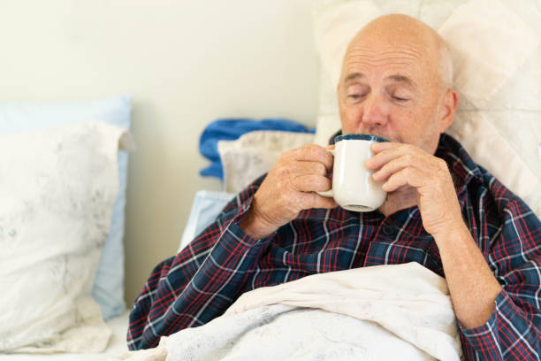 istock Senior man sick in bed having a hot drink 1214579843