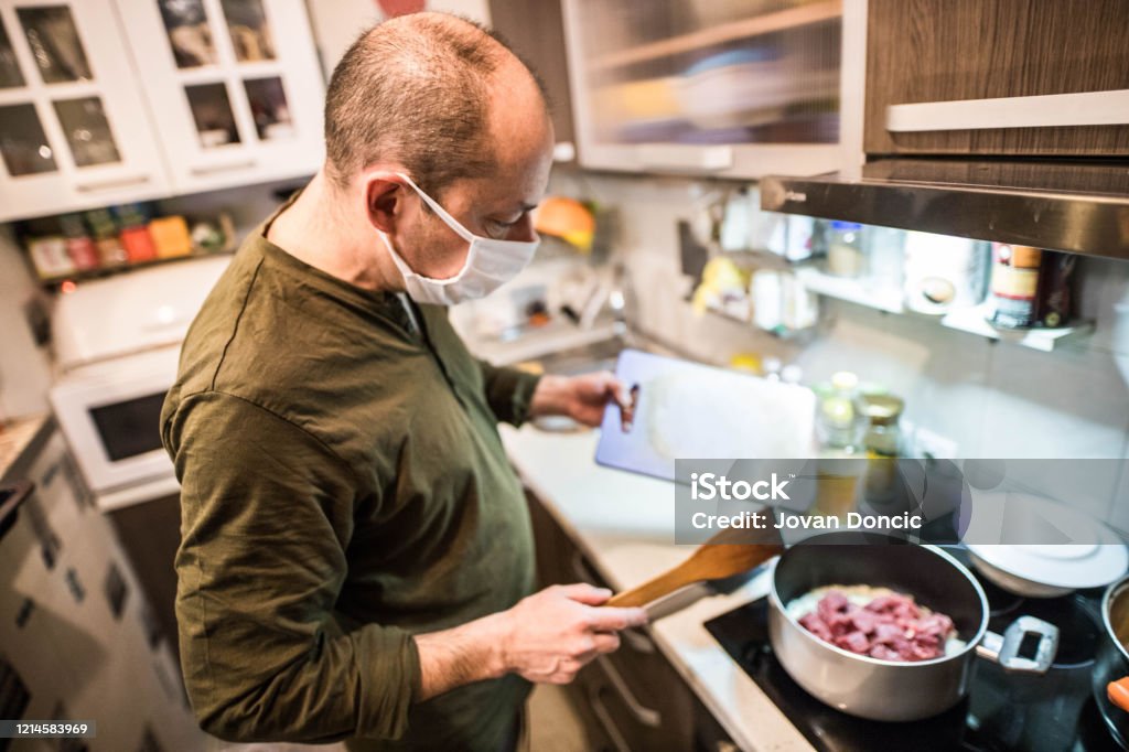 Man is cooking whit mask while covid 19 Senior man is cooking with mask  while in country is dangerous situation about covid 19 corona virus Adult Stock Photo