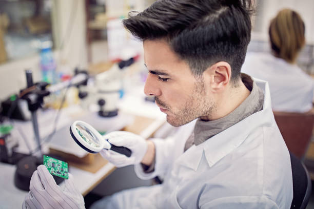 l’homme examine le circuit board dans une usine - male magnifying glass caucasian technician photos et images de collection