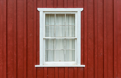 Facade with red brown colored wood and a white window frame with curtain, Telegraph Cove, Vancouver Island, British Columbia, Canada.