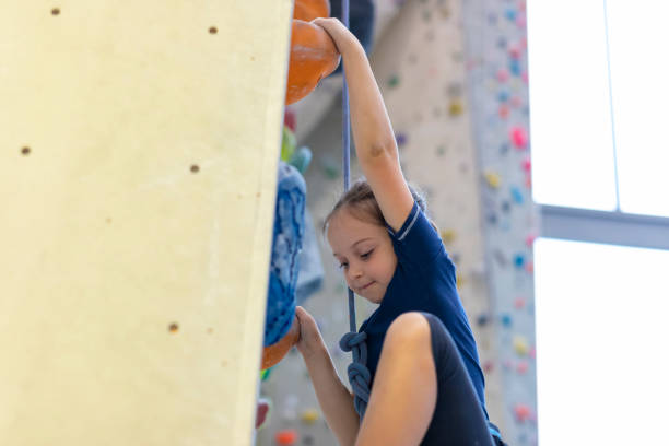 Side view of skilled 7 year old Caucasian boy gripping hand and foot holds while planning his ascent up climbing wall in modern indoor gym.