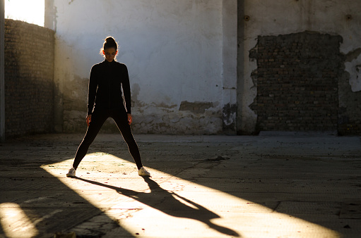 Silhouette of ballerina dancing in an abandoned building on a sunny day.