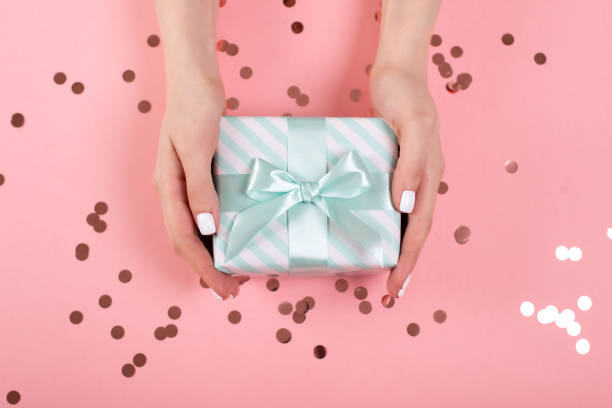 istock Womans hands holding gift or present box decorated confetti on pink pastel table top view. Flat lay composition for birthday or wedding. 1214593888