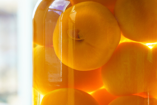 Orange Colored Peaches in Glass Jar Detail - Round spheres of fruit suspended in water solution.