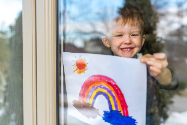 Young Boy sticking his drawing on home window during the Covid-19 crisis Young Boy sticking his drawing on home window during the Coronavirus Covid-19 crisis, Many people are putting a rainbow to tell neighbors that people inside this house are ok. #Stay at home. drawing art product photos stock pictures, royalty-free photos & images