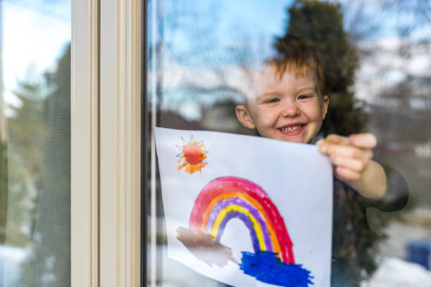Young Boy sticking his drawing on home window during the Covid-19 crisis Young Boy sticking his drawing on home window during the Coronavirus Covid-19 crisis, Many people are putting a rainbow to tell neighbors that people inside this house are ok. #Stay at home. lockdown viewpoint photos stock pictures, royalty-free photos & images