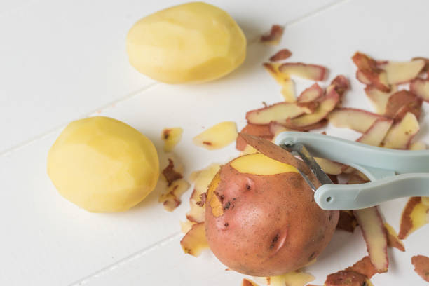 istock Peeler and potatoes on a white wooden table. 1214607377