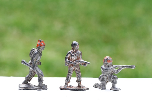 Three vintage, toy, hand made, lead soldiers. Standing figurine holding machine gun, kneeling soldier aiming rifle, and marching soldier. Remnants of hand painted colors are visible.