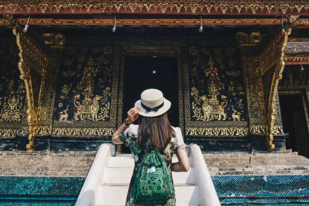 Photo of Back view of woman tourist visiting Wat Xieng Thong an iconic temple in Luang Prabang, the UNESCO world heritage town in north central of Laos.