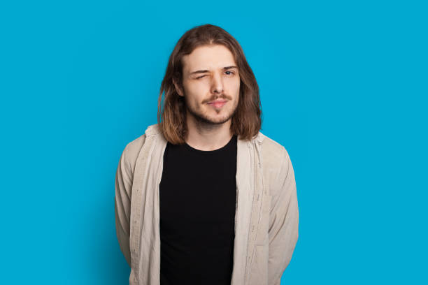 istock Bearded caucasian man with long hair is blinking while posing on a blue background 1214616416