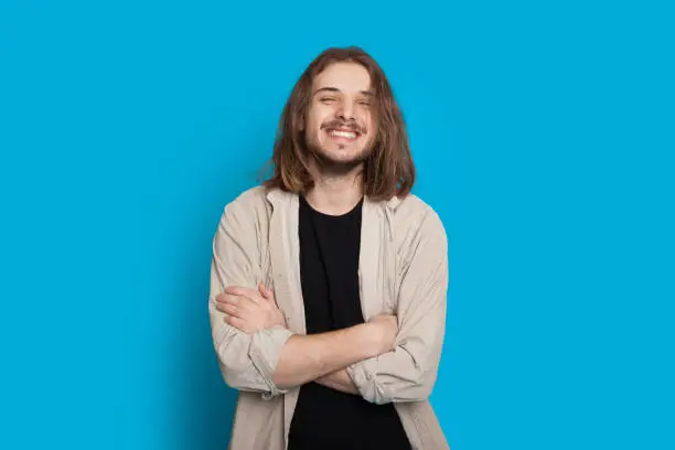 Confident caucasian man posing with crossed arms while smiling on a blue background