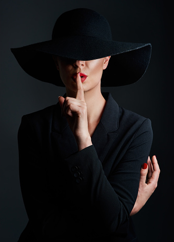 Studio shot of a beautiful mature woman wearing a hat and posing with her finger on her lips against a dark background