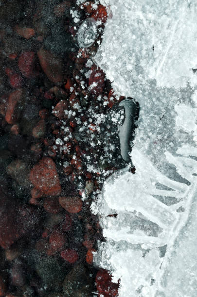 river stones covered with thin transparent ice and snow large snow crystals on ice the ice texture is vertical