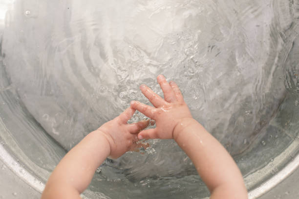 Baby Washing Their Hands in a Tub of Water. Baby girl washing her hands in a galvanized tub of water.