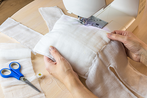 woman making home made breathing mask, corona virus protection. Homemade medical mask in the process. Sewing virus face mask at home. Detail on sewing machine.