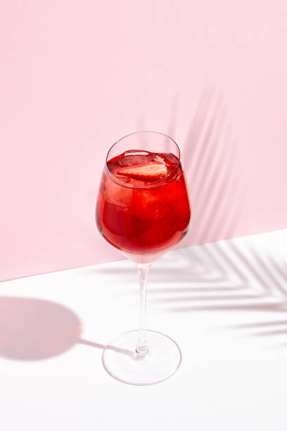 Red summer cocktail in wine glass on creative background Red summer cocktail in wine glass on creative background. Shadows of palm leaf on pink wall and white floor. red drink stock pictures, royalty-free photos & images