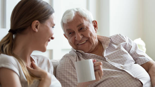 Smiling older father and adult daughter chatting at home Close up smiling older father and adult daughter chatting, drinking tea or coffee, sitting on cozy couch at home, positive mature grandfather and young woman having fun, talking, sharing news father daughter 80s stock pictures, royalty-free photos & images