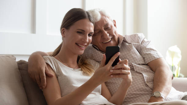 smiling older father with adult daughter using phone together - aging process middle women men imagens e fotografias de stock