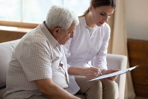 serious female doctor filling older patient checkup form during visit - aging process middle women men imagens e fotografias de stock