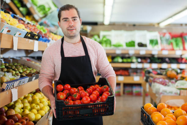 istock Young salesman holding box of  tomatoes during work 1214632555