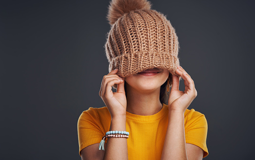 Cropped shot of an unrecognizable teenage girl wearing a beanie and feeling playful against a dark studio background