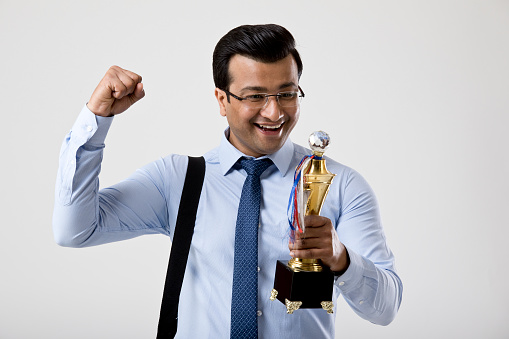 Excited businessman holding a trophy over white background