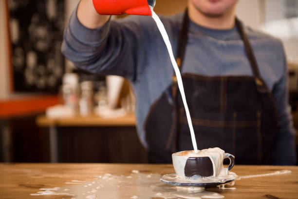 Close up barista pouring too much milk in coffee cup, making latte art