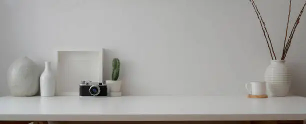 Cropped shot of minimal workspace with camera, decorations and copy space on white table with white wall