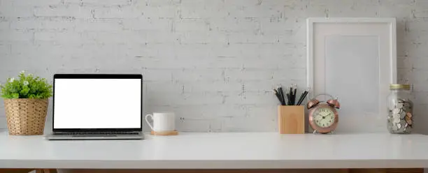 Cropped shot of simple workspace with mock-up laptop, stationery, decorations and copy space on white table with brick wall