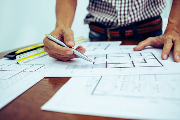 istock Close-up hand of male Architect drawing blueprint on work space in construction site. 1214645019